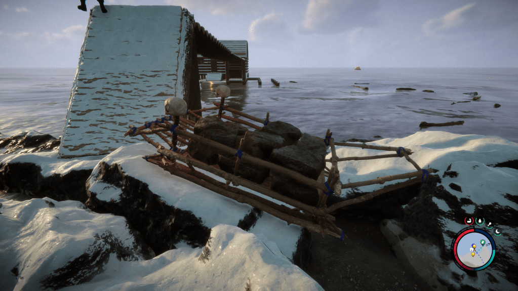 A sled made of sticks with two skull headlights sitting on a rocky shore. Landscape is coastal with snow covering the rocks. In the sled is a pile of large stones.